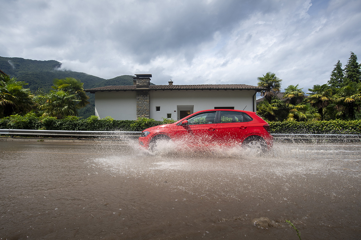 [Symbolbild] Ein Personenwagen fährt am 27. Juli 2021 in Melano, Tessin, auf einer überschwemmten Strasse. Entscheidend beim Durchqueren von Wasser ist nicht die Art des Antriebs, sondern die sogenannte Wattiefe durch die ein Fahrzeug fahren kann. Foto: Keystone-SDA / Pablo Gianinazzi